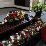 Funeral casket surrounded by red and white flowers.