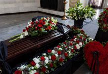 Funeral casket surrounded by red and white flowers.