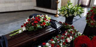 Funeral casket surrounded by red and white flowers.