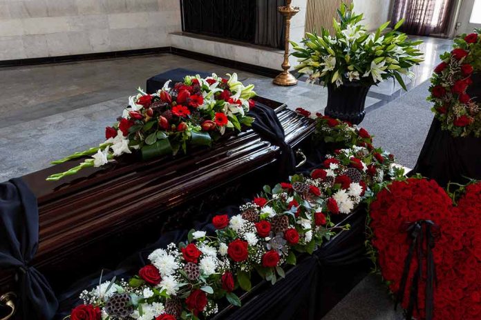 Funeral casket surrounded by red and white flowers.