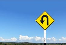 Yellow uturn sign against blue sky