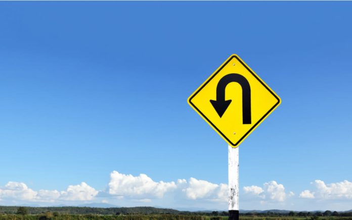 Yellow uturn sign against blue sky