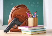 Gun and backpack on desk with school supplies.