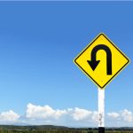 Yellow uturn sign against blue sky