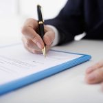 Person signing a document with a black pen.