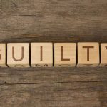 Wooden blocks spell out "GUILTY" on wood background.