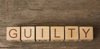 Wooden blocks spell out "GUILTY" on wood background.