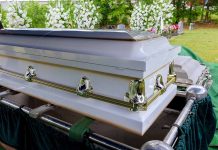 White coffin with flowers in the background.