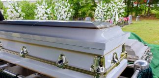 White coffin with flowers in the background.