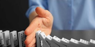 Hand stopping falling row of dominoes.