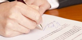 Hand signing a document with a pen.