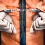 Hands cuffed behind bars in prison uniform