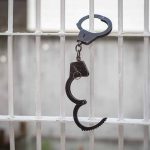 Open handcuff hanging on white prison bars