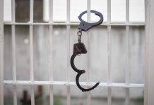 Open handcuff hanging on white prison bars