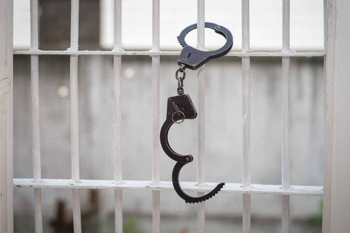 Open handcuff hanging on white prison bars