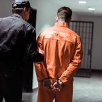 Policeman escorting handcuffed prisoner in orange jumpsuit