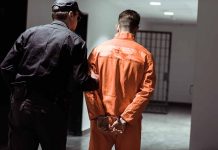 Policeman escorting handcuffed prisoner in orange jumpsuit