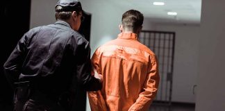 Policeman escorting handcuffed prisoner in orange jumpsuit