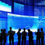 Silhouetted people in front of stock market displays