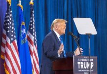 Person speaking at podium with flags in background
