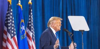 Person speaking at podium with flags in background