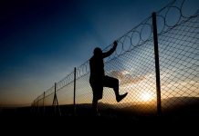 Silhouette of person climbing barbed wire fence at sunset