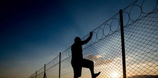 Silhouette of person climbing barbed wire fence at sunset