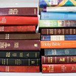 Several Bible editions stacked on a bookshelf