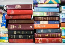 Several Bible editions stacked on a bookshelf