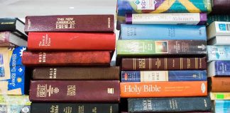 Several Bible editions stacked on a bookshelf