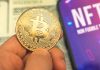 Person holding Bitcoin coin, NFT text on screen