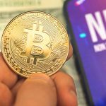 Person holding Bitcoin coin, NFT text on screen