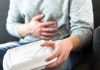 Person holding stomach with one hand, food container in other.