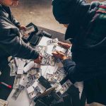 Two individuals handling stacks of money on a table