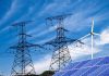 Solar panels and a wind turbine with power lines against a blue sky