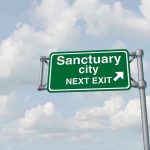 Green road sign saying sanctuary city next exit