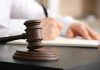 Judge's gavel on desk with person writing.