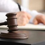 Judge's gavel on desk with person writing.
