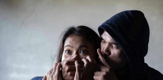 Man holding womans mouth, gesturing silence.