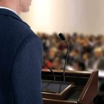 A speaker at a podium addressing an audience
