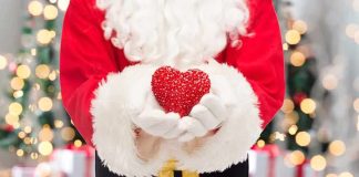 Santa Claus holding a red heart in front of a festive background