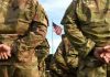 Soldiers stand in formation with American flag in background