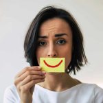 Woman holding smiley face card over mouth