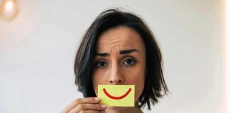 Woman holding smiley face card over mouth