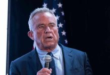 Man holding microphone speaking with American flag behind