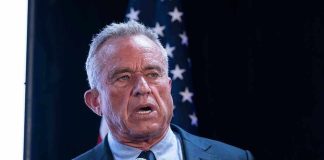 Man holding microphone speaking with American flag behind