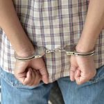 A person in handcuffs viewed from behind wearing a plaid shirt and denim jeans