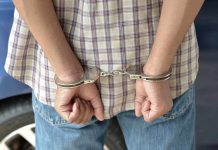 A person in handcuffs viewed from behind wearing a plaid shirt and denim jeans