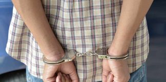 A person in handcuffs viewed from behind wearing a plaid shirt and denim jeans