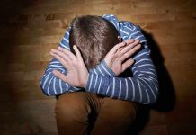 A child sitting on the floor with their hands covering their face expressing distress